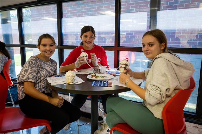 Three students smile while sitting at a table